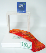 Load image into Gallery viewer, A_folded_red_and_orange_painted_silk_scarfwith_a_Louise_Loughman_artist_swing_tag_draped_over_a_white_display_stand_with_the_Made_Local_You_Can_Own_It_card_against_a_white_background.