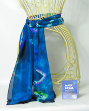 Load image into Gallery viewer, silk_scarf_in_shades_of_blue_tied_around_a_wire_mannequinn_worn_as_a_belt_with_the_madlocal_sign