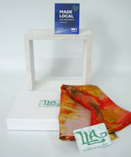 Load image into Gallery viewer, silk_scarf_folded_on_a_gift_box_in_colours_of_red_and_gold_with_the_made_local_sign_and_louise_loughman_artist_cards