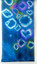 Load image into Gallery viewer, A_vertical_section_of_silk_scarf_showing_tye_dye_design_diamond_shapes_and_a_heart_shape_with_textured_whites_and_little_flashes_of_colour_against_a_white_wall
