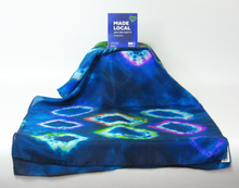 Load image into Gallery viewer, A_blue_scarf_with_a_colorful_tie_dye_pattern_of_hexagonal_diamond_like_shapes,_draped_to_show_its_design,_with_a_small_blue_'MADE LOCAL'_card_standing_on_top_against_a_white_background.
