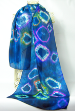 Load image into Gallery viewer, A_sheer_blue_scarf_with_a_tie_dye_style_geometric_pattern_in_purple,_pink,-green,_and_white,_draped_on_a_cream_colored_mannequin_against_a_white_background.
