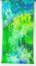 Load image into Gallery viewer, A_section_of_silk_scarf_featuring_a_vibrant_hand_tie_dye_pattern_in_green,_blue_and_yellow_with_a-handpainted_spiral_design_inspired-by_the_carvings_found_at_Newgrange_displayed_up_against_a_white_background
