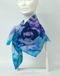 a_silk_scarf_hand_painted_with_celtic_design_at_frontign_blues_lilacs_violet_bright_aqua_scarf_tied_around_neck_showing_spiral_design