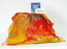 Load image into Gallery viewer, A_silk_scarf_in_vibrant_gold_and_red_shades_draped_over_cube_depeicting_the_wax_drawing_of_the_gold_finch_with_the_made_local_sign_and_the_Louise_loughman_artist_logo
