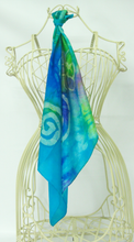 Load image into Gallery viewer, silk_square_hanging_from_the_cream_coloured_wire_mannequin_in_shades_of_turquoise_blue_green_and_yellow
