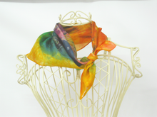 Load image into Gallery viewer, A_silk_scarf_with_a_vibrant_multicolor_gradient_pattern_of_yellow,_green,_orange,_and_purple,_tied_in_a_knot_and_displayed_on_a_cream_colored_wire_mannequin_bust_against_a_white_background.
